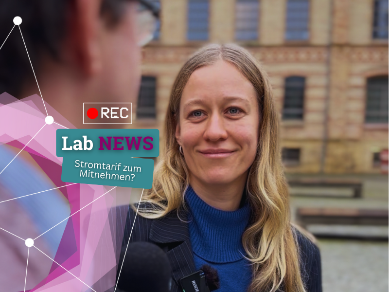 Eine Frau mit langem blonden Haar trägt einen schwarzen Blazer und einen blauen Rollkragenpullover und steht vor einem Gebäude