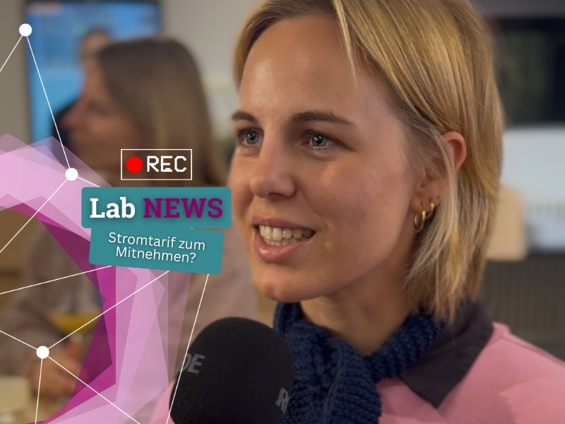 Person mit blonden Haaren und blauem Schal hält ein Mikrofon mit der Aufschrift 'RDE' in einem Studio mit unscharfem Hintergrund
