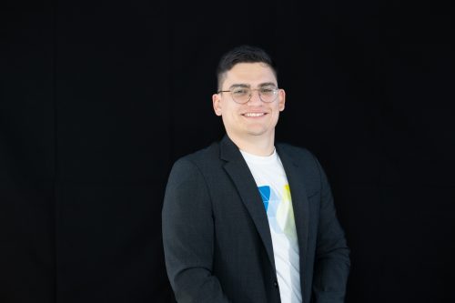 Mann in schwarzem Sakko und weißem T-Shirt vor schwarzem Hintergrund