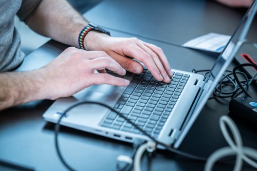 Hände tippen auf einer Laptop-Tastatur mit einem bunten Armband am linken Handgelenk