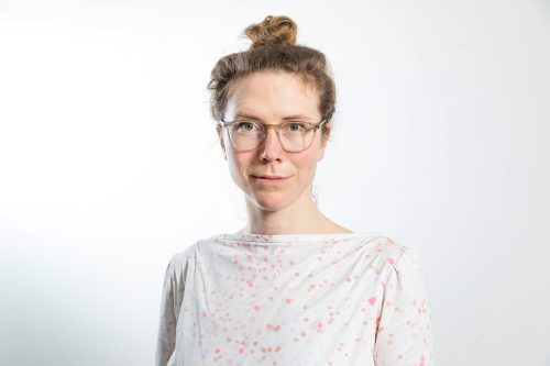 Frau mit hochgestecktem Haar und weißem Oberteil mit buntem Tupfenmuster vor hellem Hintergrund