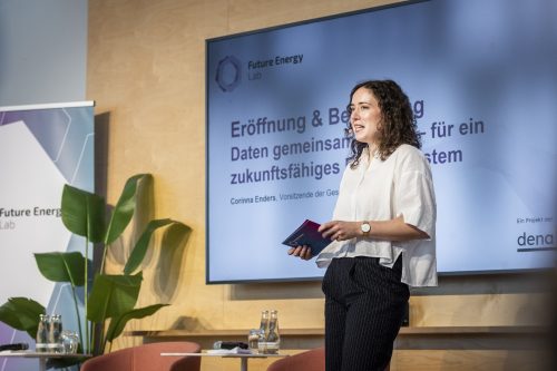 Frau steht vor großem Bildschirm mit Text und hält Notizbuch in der Hand