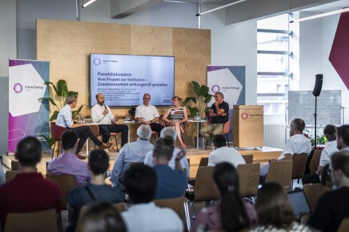 Podiumsdiskussion mit fünf Personen auf einer Bühne vor Publikum in einem modernen Veranstaltungsraum