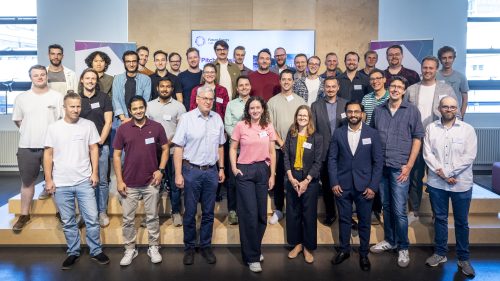 Gruppenfoto von mehreren Personen in einem Raum mit Präsentationsbildschirm und Bannern im Hintergrund