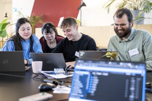 Vier Personen sitzen an einem Tisch mit Laptops und konzentrieren sich auf die Bildschirme mit fröhlichen, lachenden Gesichter.