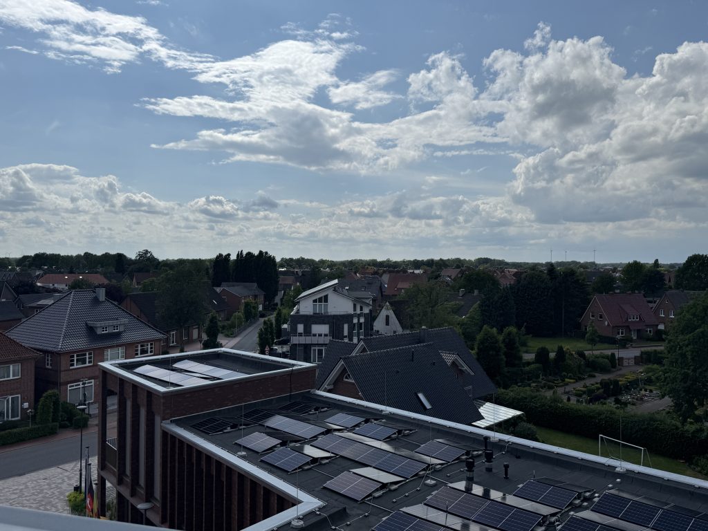 Blick über ein Wohngebiet mit Häusern und einem Gebäude mit Solarpaneelen auf dem Flachdach unter einem bewölkten Himmel