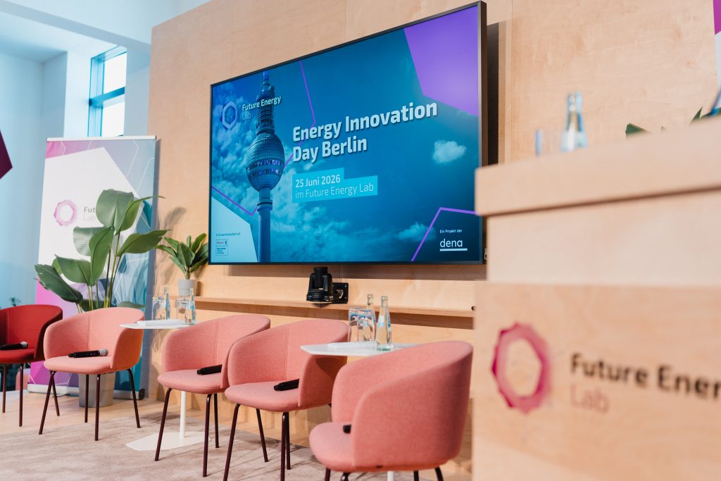 Moderner Veranstaltungsraum mit rosa Sesseln, Pflanzen und großem Bildschirm mit der Aufschrift 'Energy Innovation Day Berlin 25 Juni 2026 im Future Energy Lab'