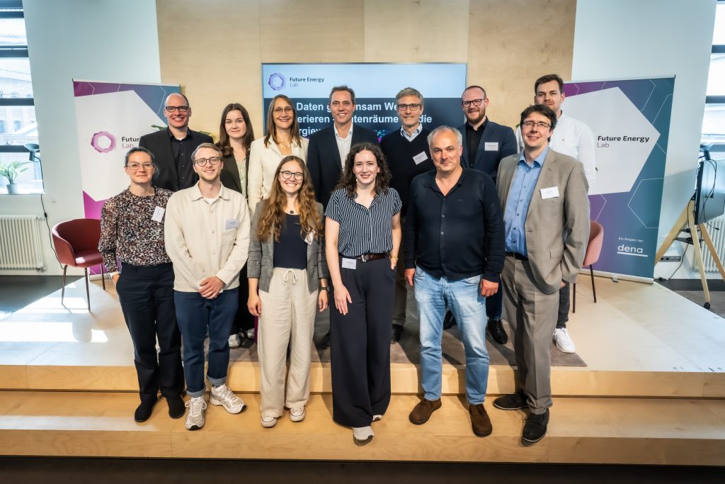 Gruppe von zwölf Personen steht in einem hellen Raum vor einem Bildschirm und zwei Bannern mit dem Schriftzug 'Future Energy'