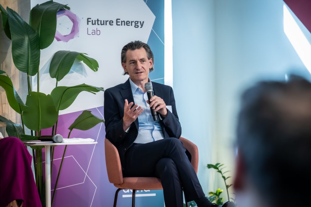 Mann in Anzug sitzt auf Stuhl und spricht mit Mikrofon vor Banner mit Schriftzug 'Future Energy Lab'