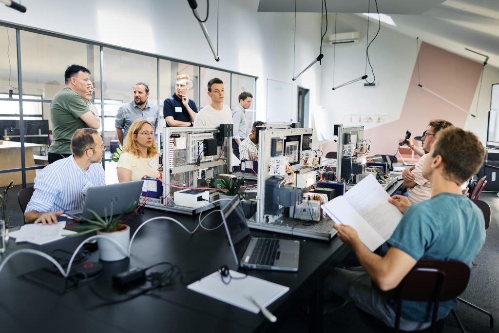 Gruppe von Menschen in einem modernen Büro, die an Computern und technischen Geräten arbeiten und sich unterhalten