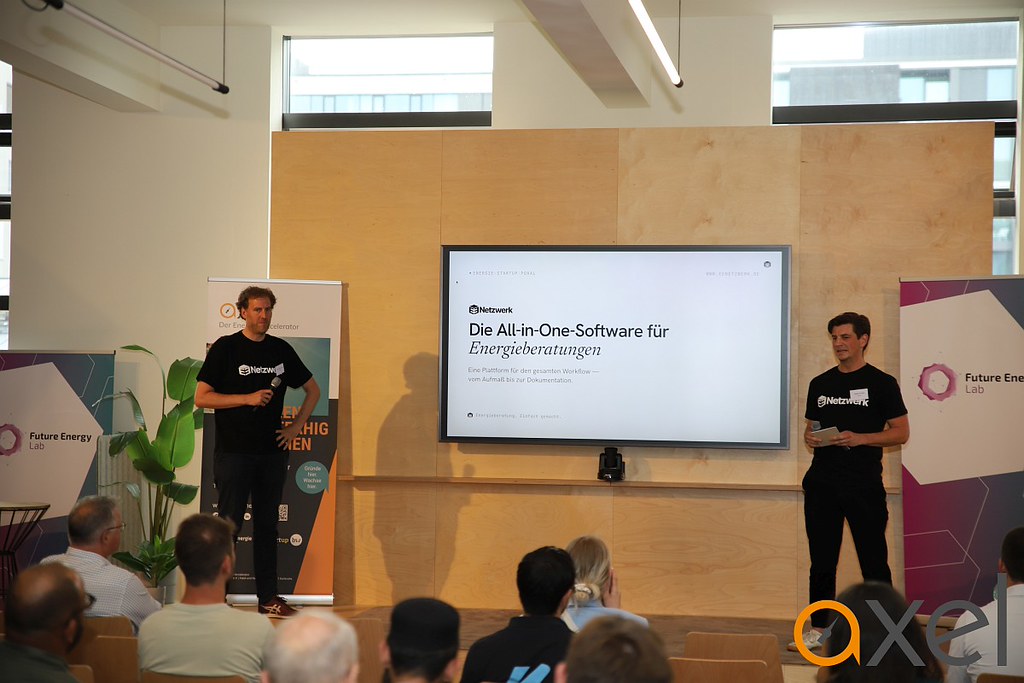 Zwei Männer in schwarzen T-Shirts präsentieren vor Publikum eine Software auf einem großen Bildschirm mit der Überschrift 'Die All-in-One-Software für Energieberatungen'