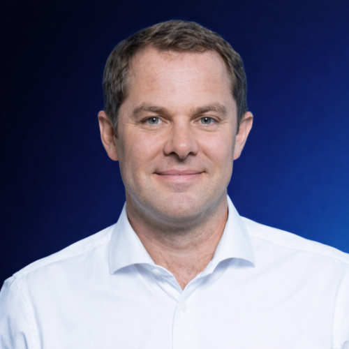 Mann mit kurzem braunem Haar und weißem Hemd vor blauem Hintergrund
